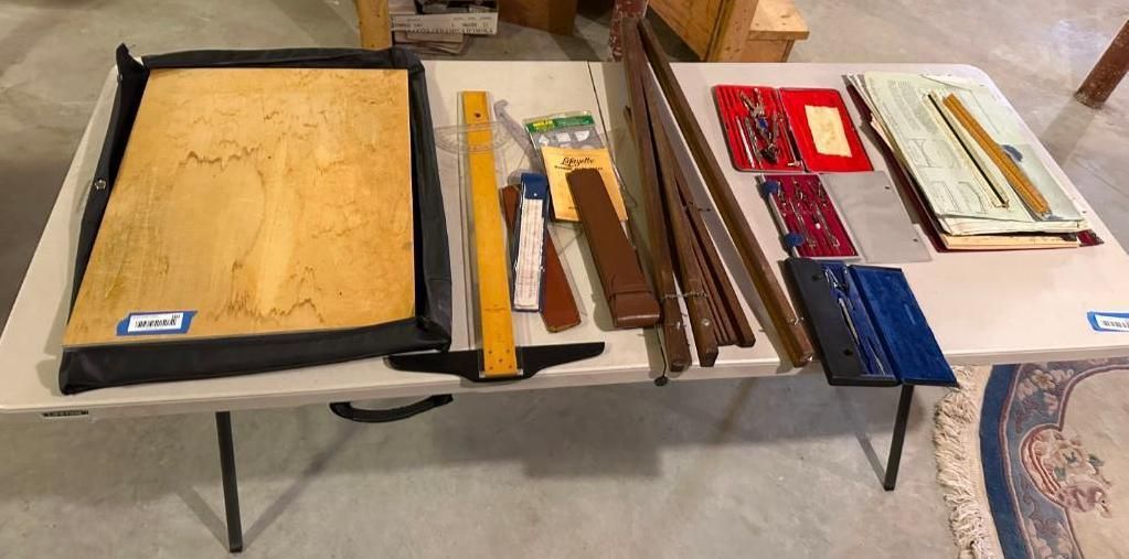 Various drafting and measuring tools on a white table: T-square, rulers, frames, slide rules, and a drawing board.