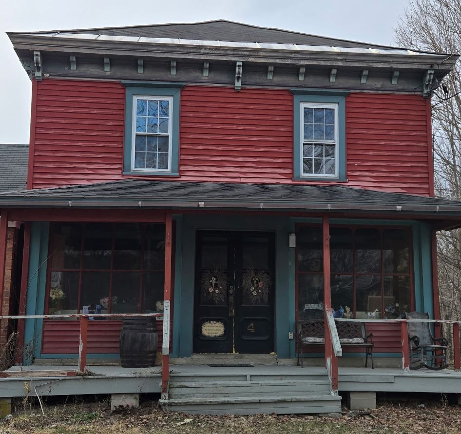 A two-story red building with a porch, blue trim, and two front glass doors, standing on a wooden deck.