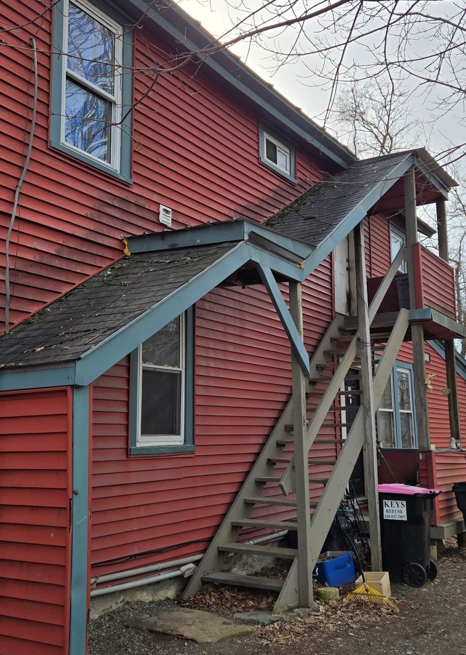 An exterior view of a red-sided house with a wooden outdoor staircase leading to a second-story entrance.