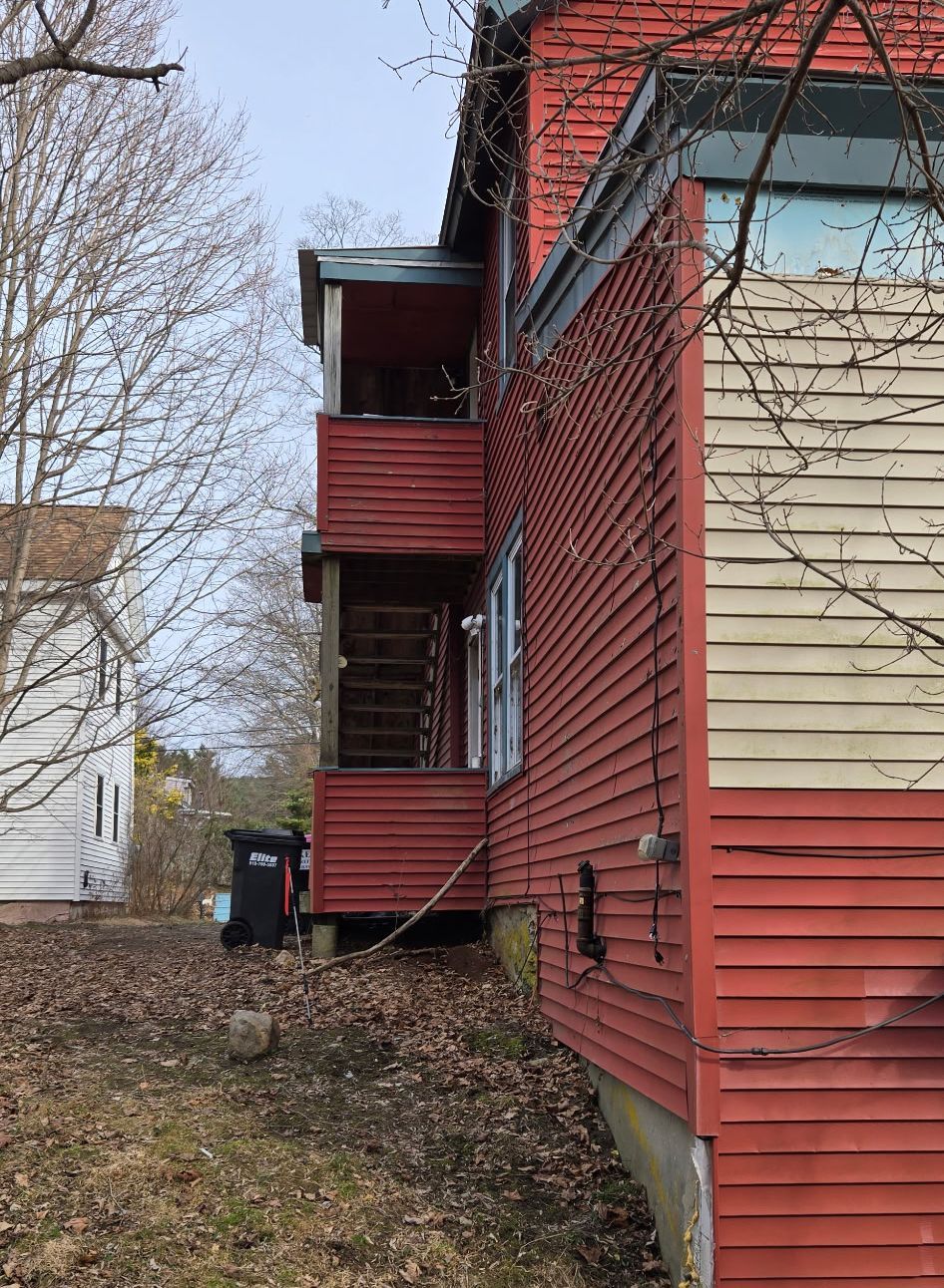 A side view of a two-story red house with a porch and wooden staircase.
