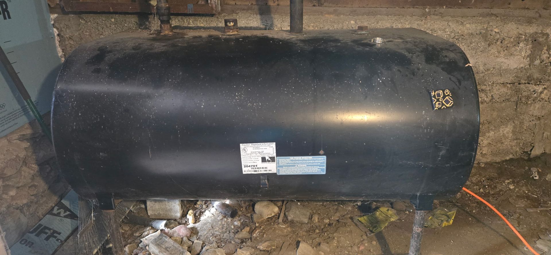 A horizontal, black cylindrical oil storage tank positioned on legs in a basement setting.