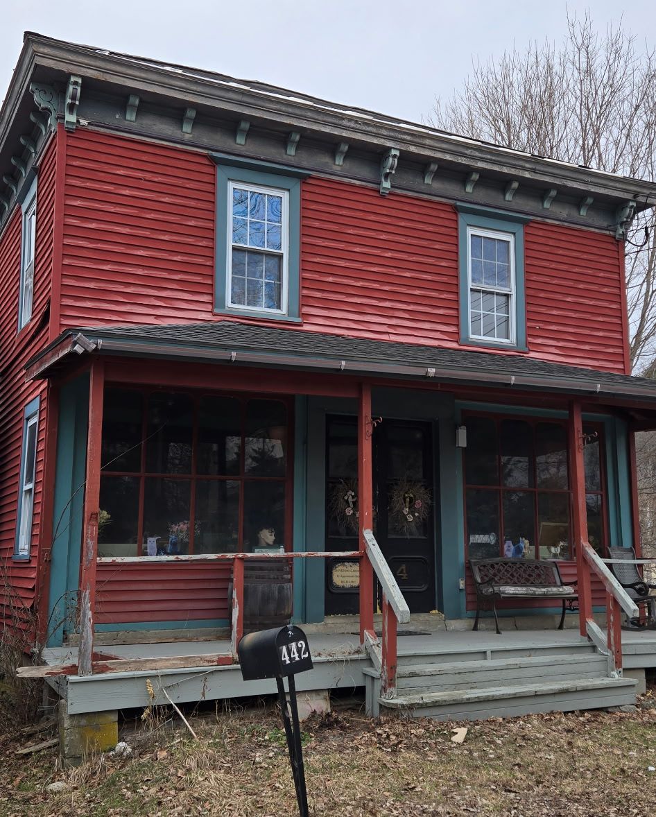 A two-story red farmhouse with a blue-trimmed porch, dark front door, and a black mailbox in the front yard.