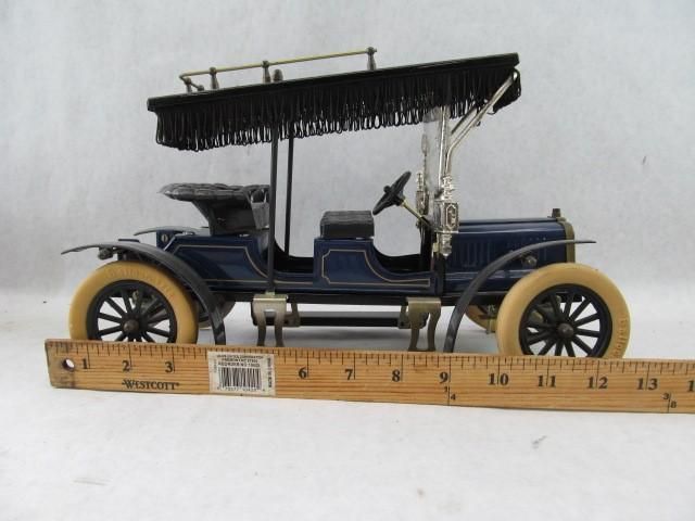 Blue and tan antique toy car with black fringed canopy, wooden ruler in front.