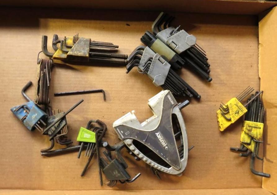 A cardboard box filled with various black hex key sets, some with holders.