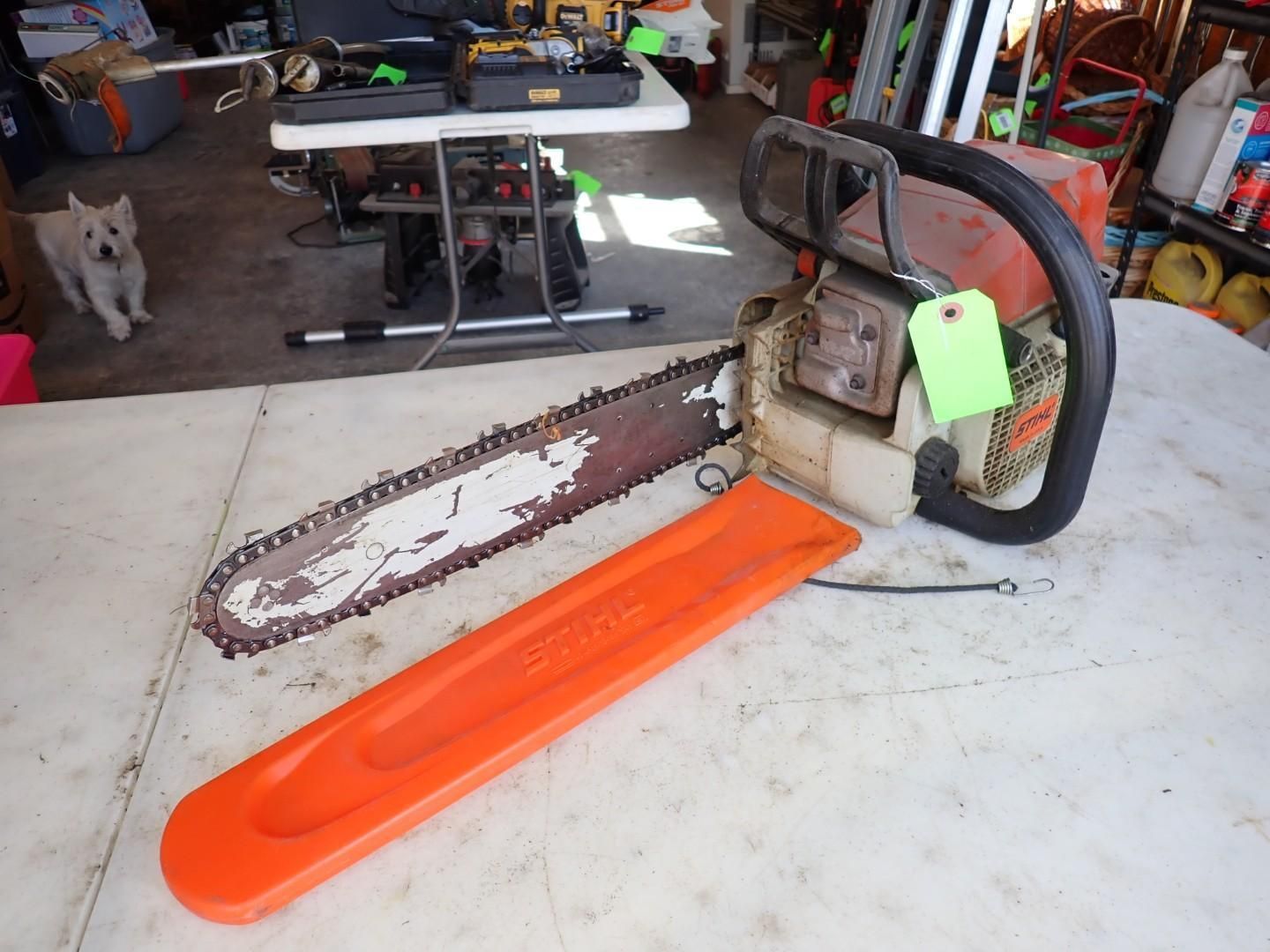 Chainsaw with orange blade cover on a workbench in a garage