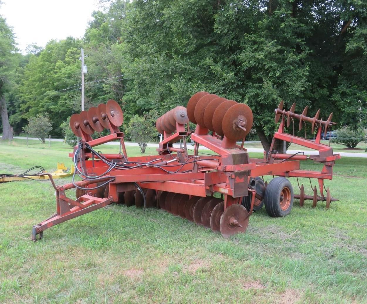 Red farm disc harrow on a grassy field, with a wheel and spikes.