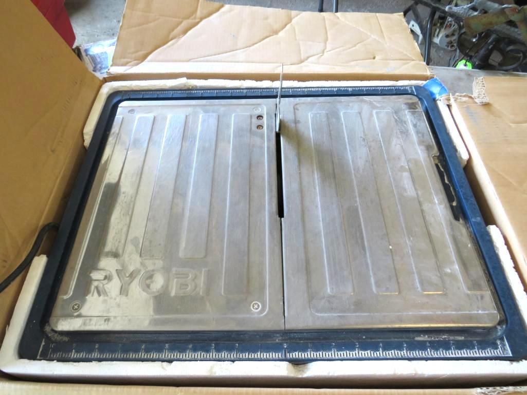 Ryobi tile saw in cardboard box. Silver blade and table with ruler along the front edge.