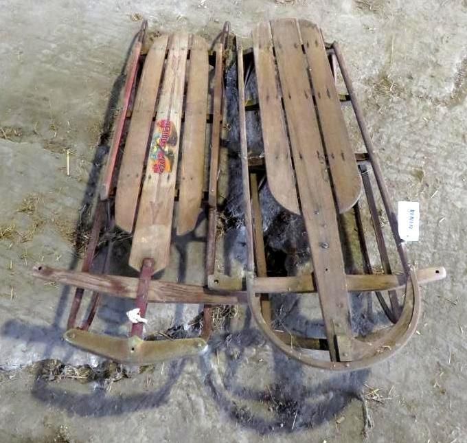 Two antique wooden sleds on a concrete surface. One has a painted design.