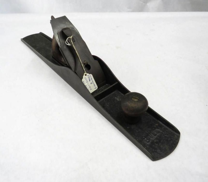A black hand plane with wooden knob and handle, sitting on a white surface.