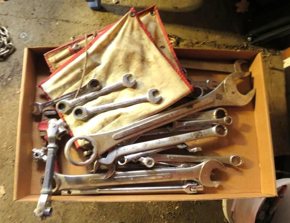 A wooden box overflowing with various wrenches and a tool roll.