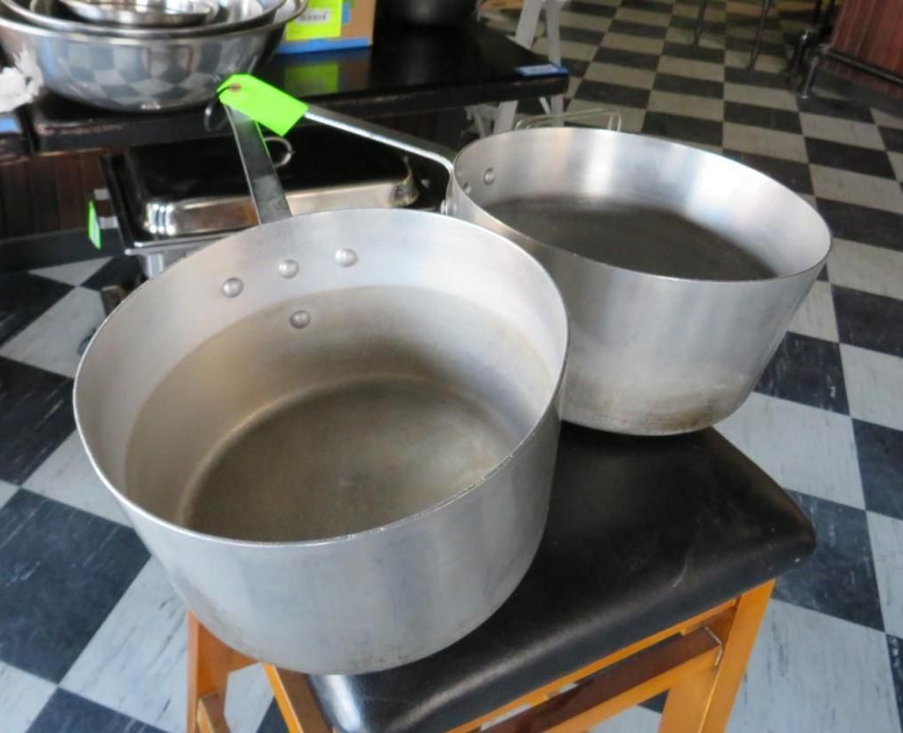 Two metal pots filled with water on a stool; one with a green-handled pan.