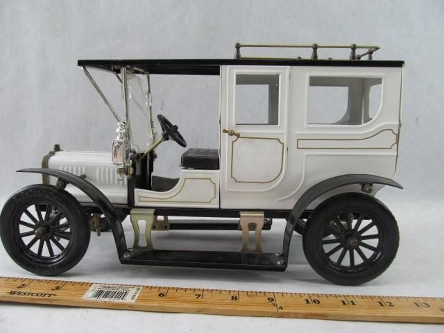 White and black model vintage car with dark wheels, open driver's seat and enclosed passenger area.