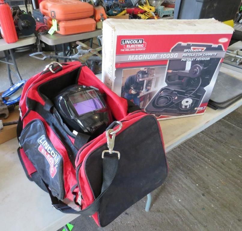 Red and black Lincoln Electric welding bag with a helmet, next to a box for a Magnum 100SD wire feeder.