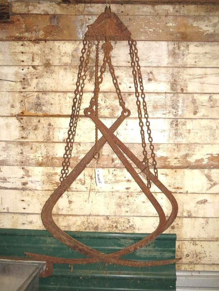 Metal logging tongs hanging in front of a wooden wall.