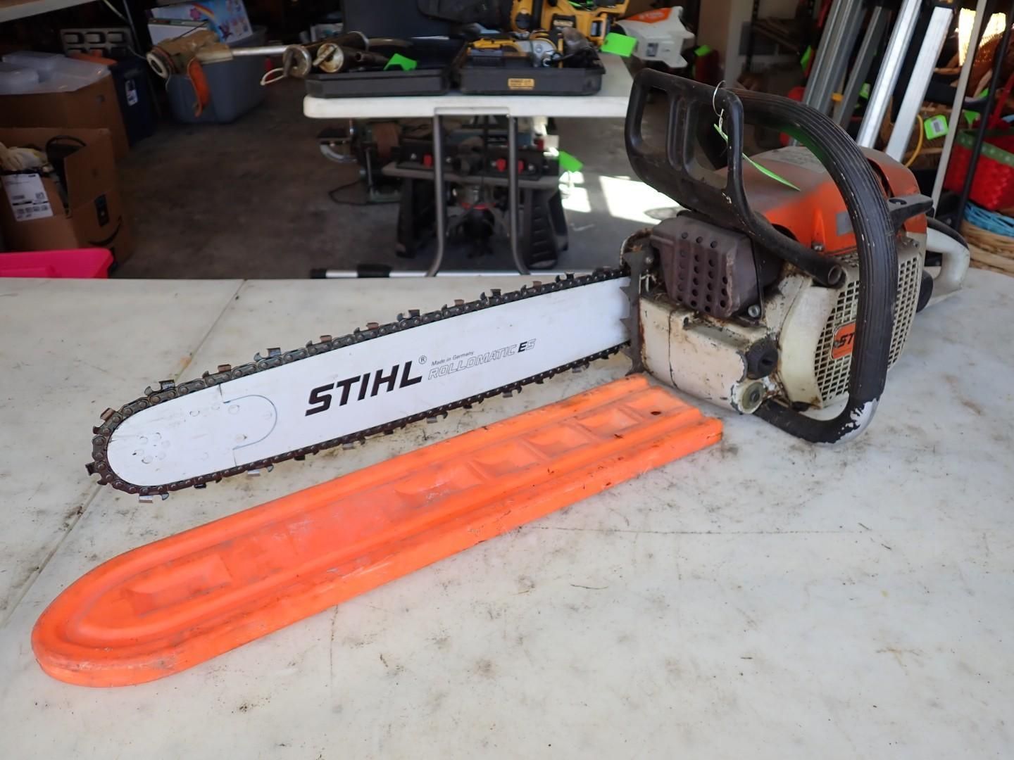Stihl chainsaw resting on an orange bar cover in a garage/workshop.