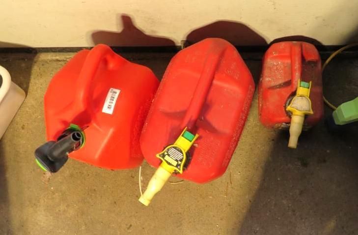 Three red gasoline containers on a concrete floor; each with a nozzle.