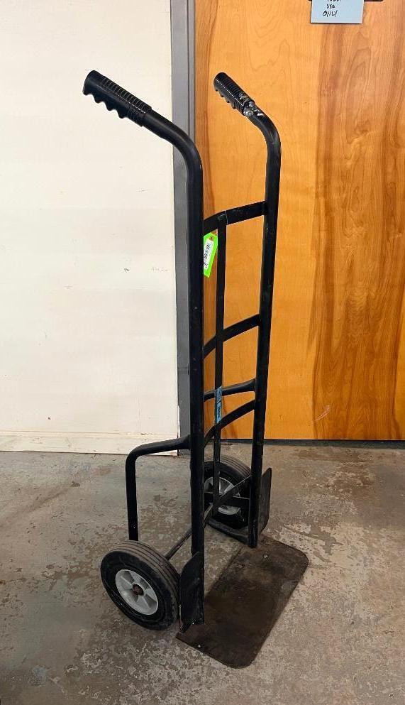 Black hand truck against a beige wall and brown door.