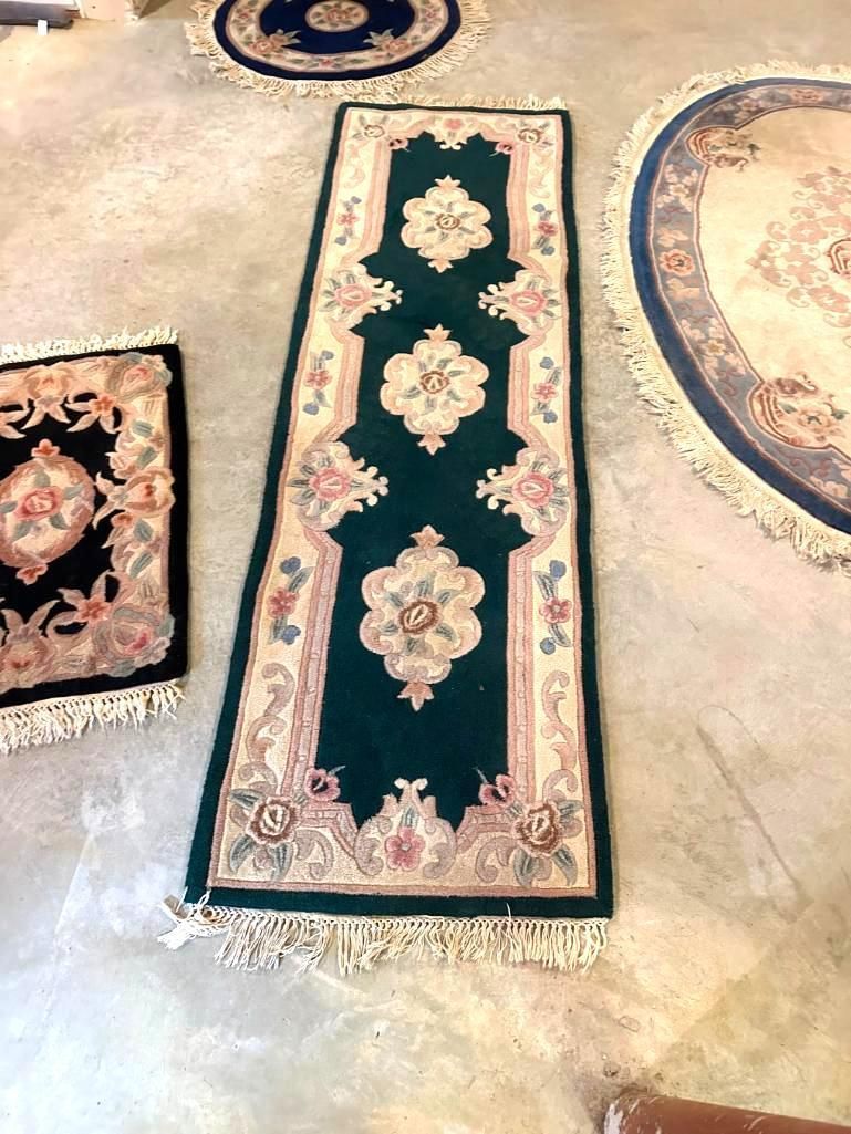 Green and pink runner rug with floral design, fringe on a concrete floor.