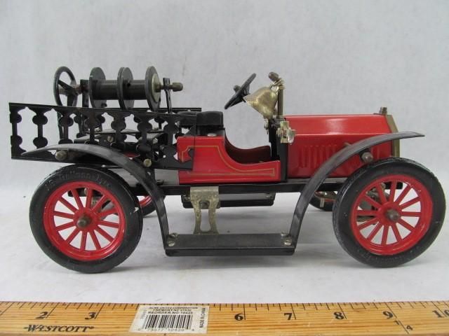 Red and black vintage toy fire truck with red spoke wheels, black detailing, and fire hose reel.