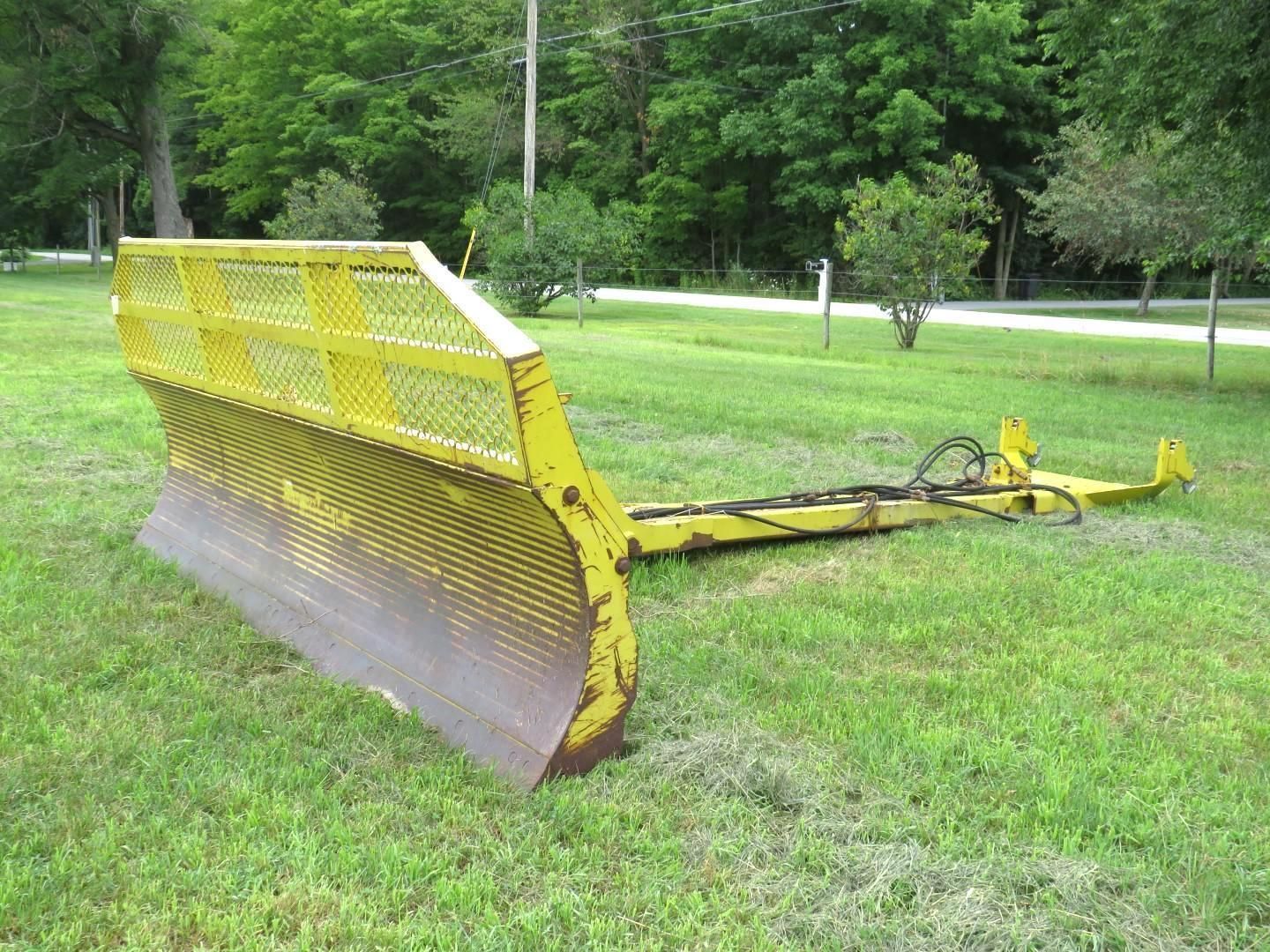 Yellow tractor blade on green grass. Metal blade with mesh top.