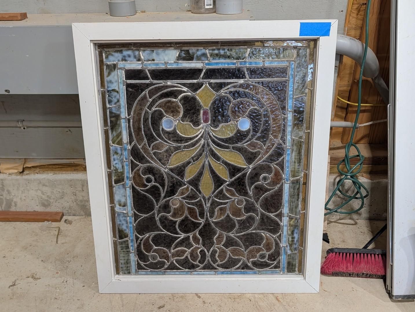 White-framed decorative metal gate or vent panel with ornate black swirls leaning against a wall outdoors