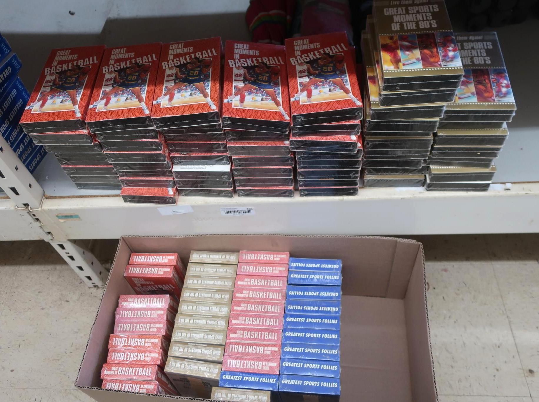 Stacks of VHS tapes on shelves and in a box, mostly red and black. Some yellow and blue tapes too.