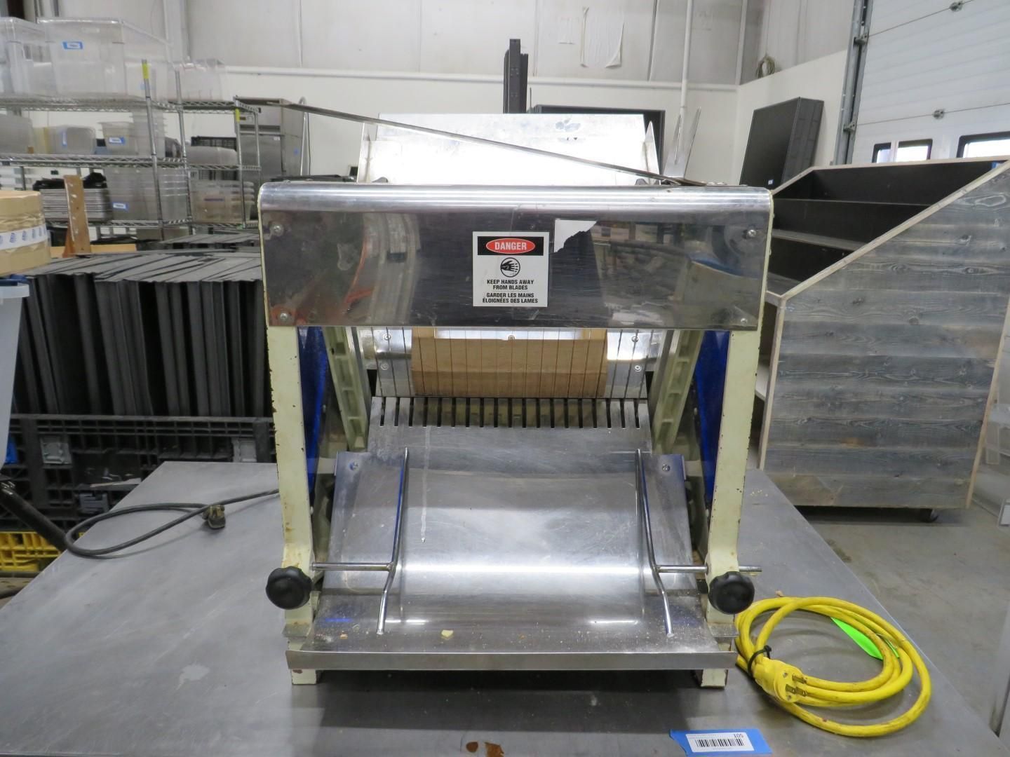 Stainless steel bread slicer on a metal table, with a yellow power cord.