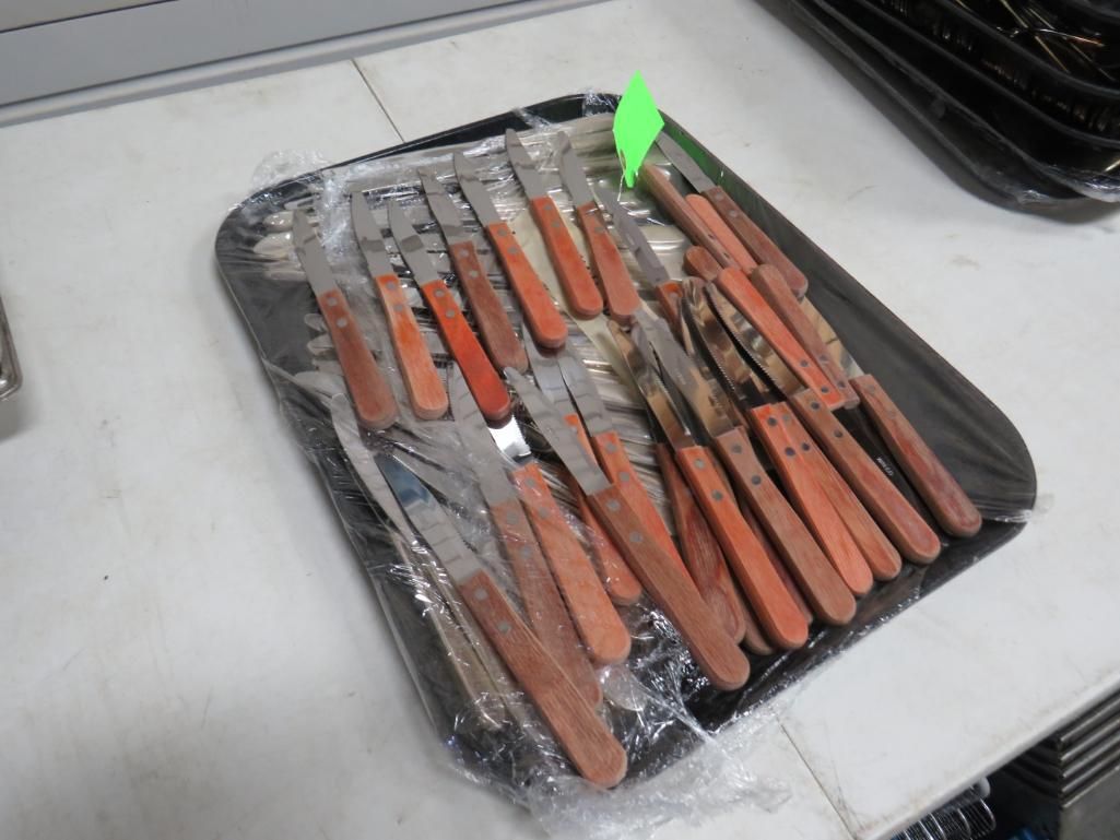 Knives with wooden handles on a black tray, wrapped in clear plastic.