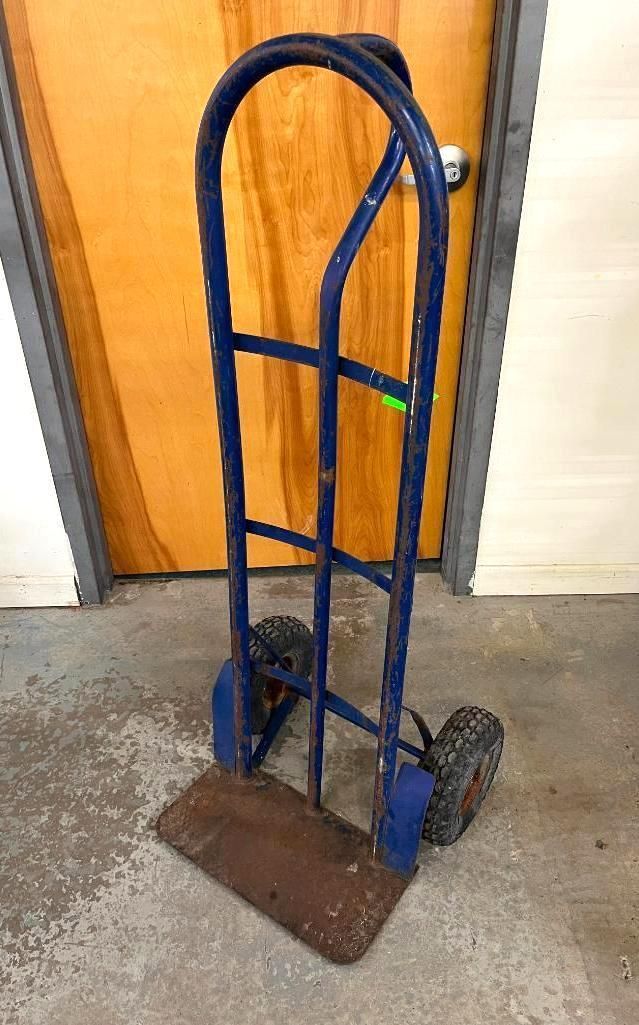 Blue hand truck with base and two wheels, set in front of a wooden door.
