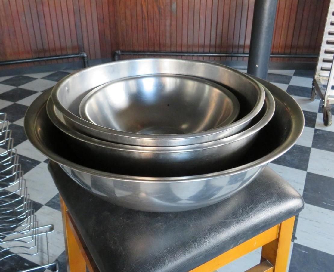 Four nested stainless steel mixing bowls on a black stool in front of a checkered floor.
