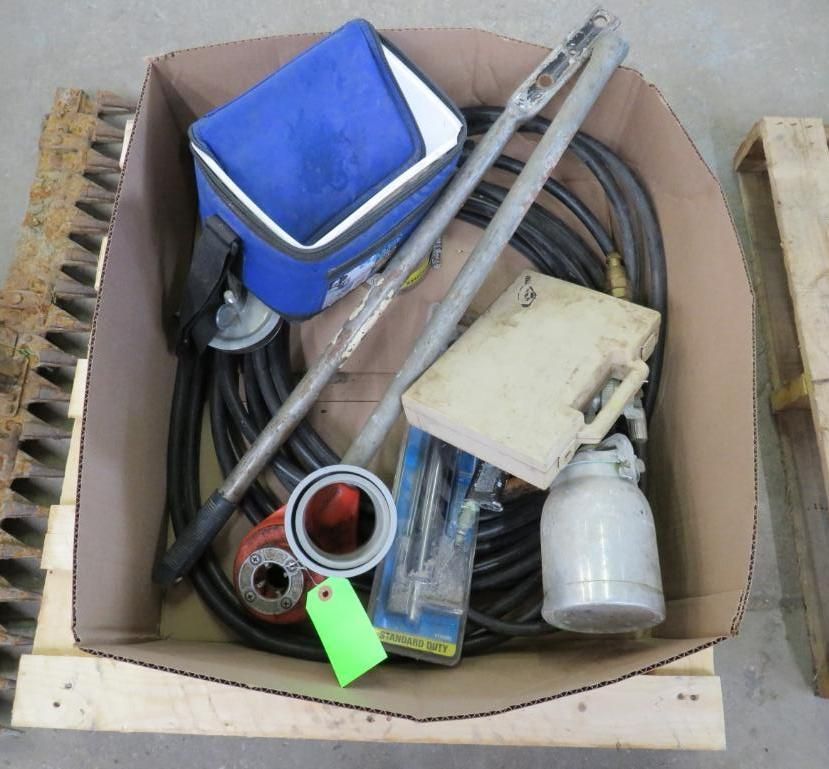 Cardboard box filled with plumbing tools: blue bag, metal pipes, spray can, and other tools.