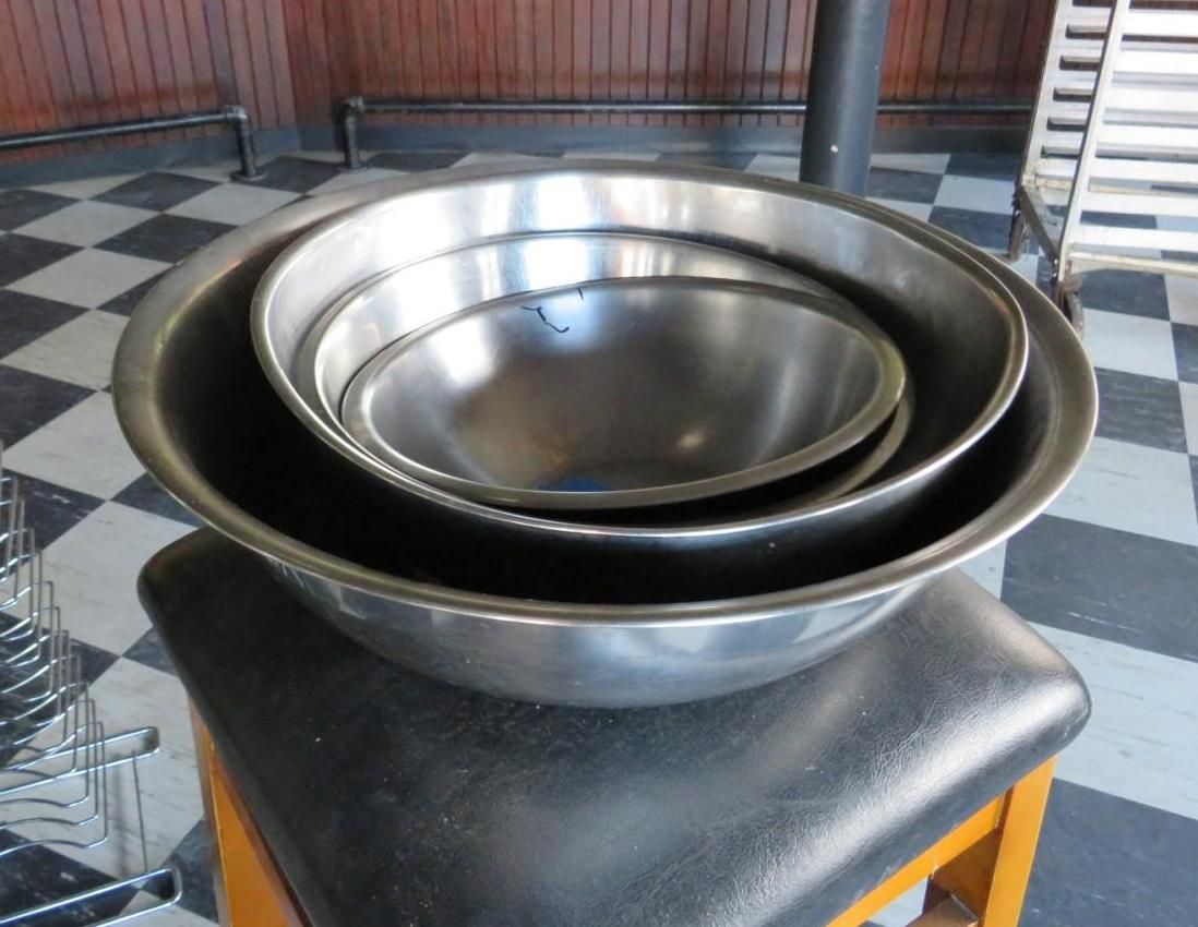 Three stainless steel mixing bowls nested on a black, cushioned stool, against a checkered floor.