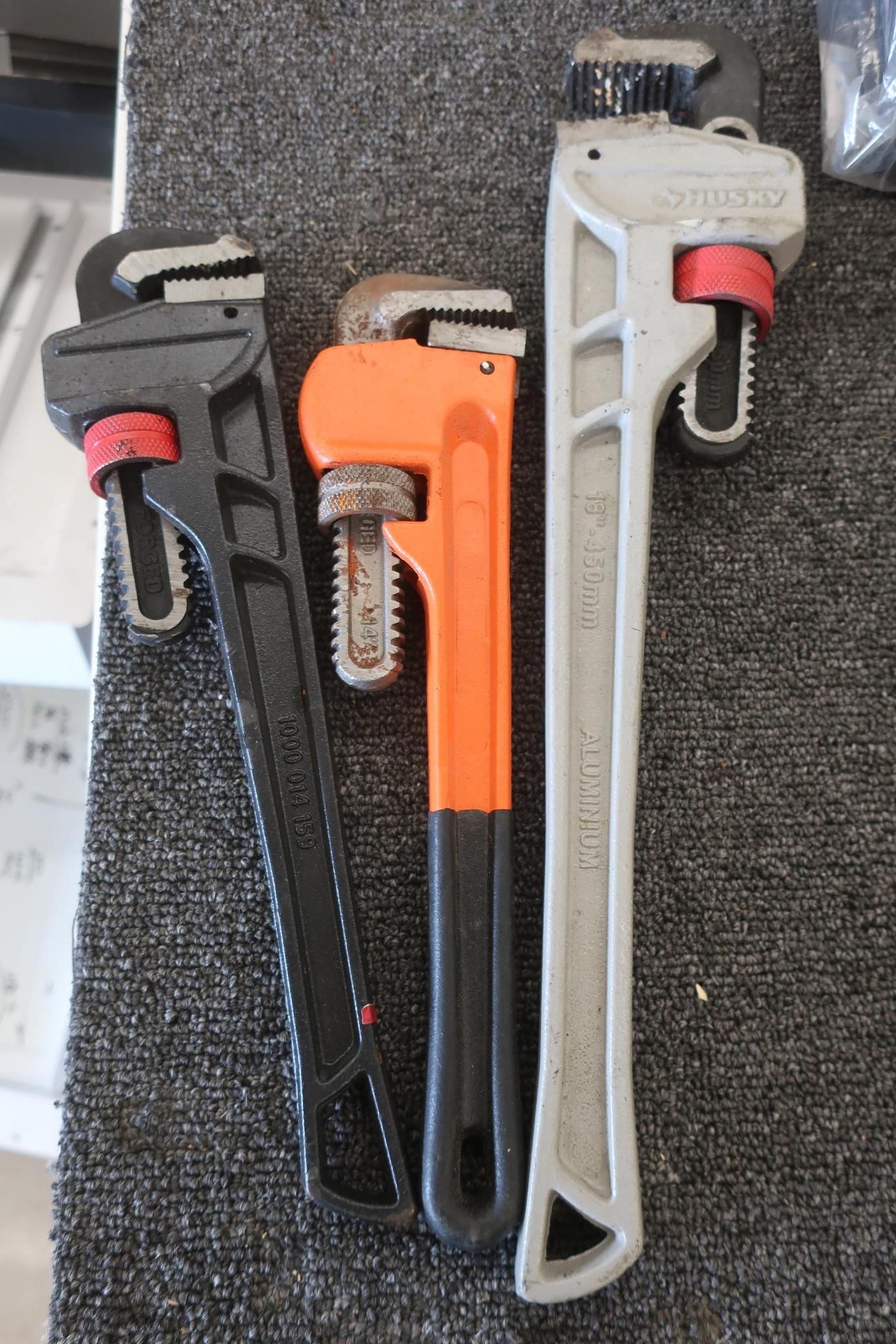Three pipe wrenches of different sizes and colors: black, orange, and gray.