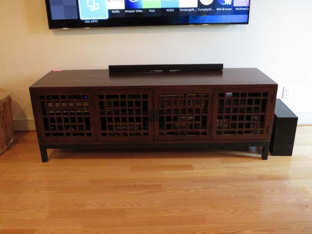 Wooden entertainment center with latticed doors, below a mounted TV, with a subwoofer.