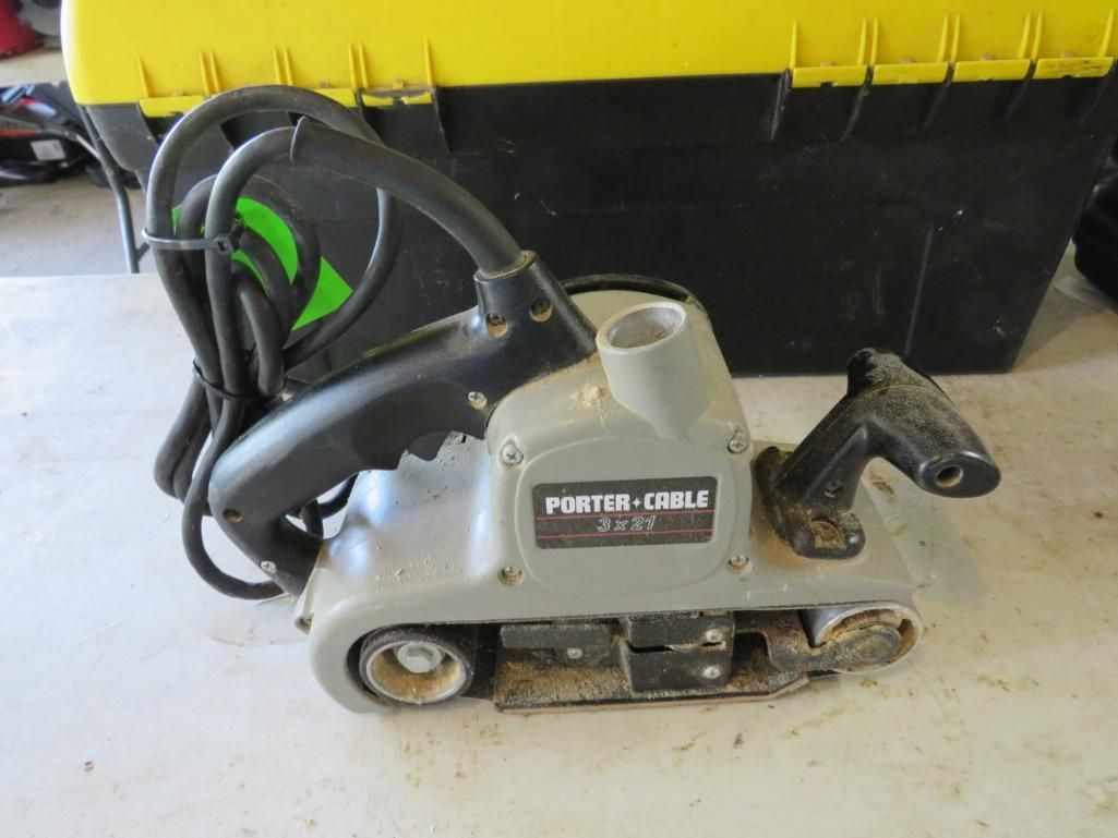 Porter-Cable belt sander, gray with black handle and cord, in front of a yellow and black toolbox.