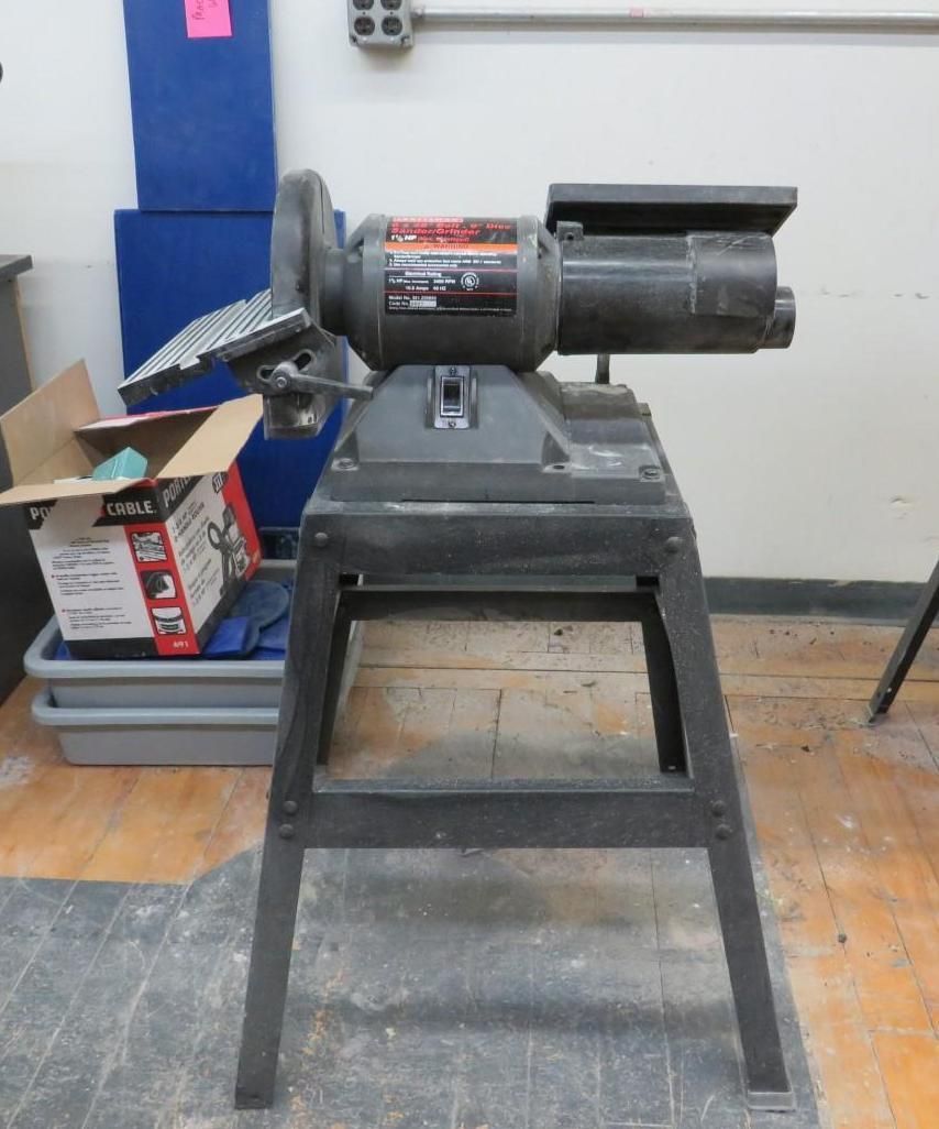 Bench grinder on a black metal stand, in a workshop setting.