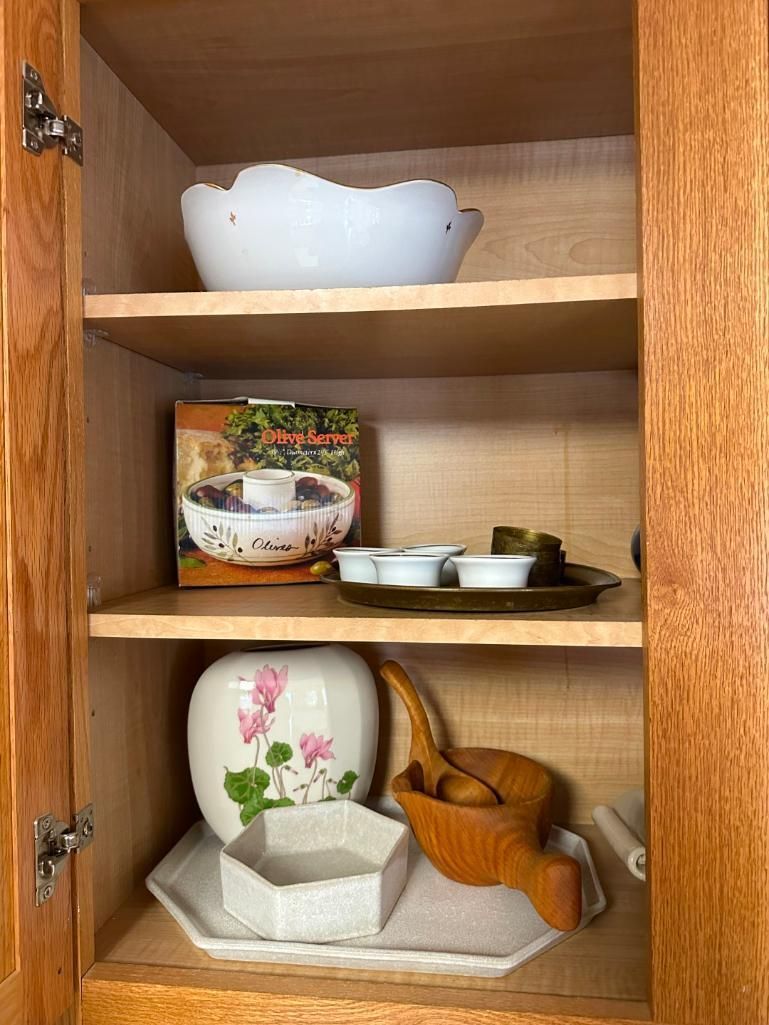 A wooden cabinet with shelves holding various white and brown dishes, a book, and decorative items.
