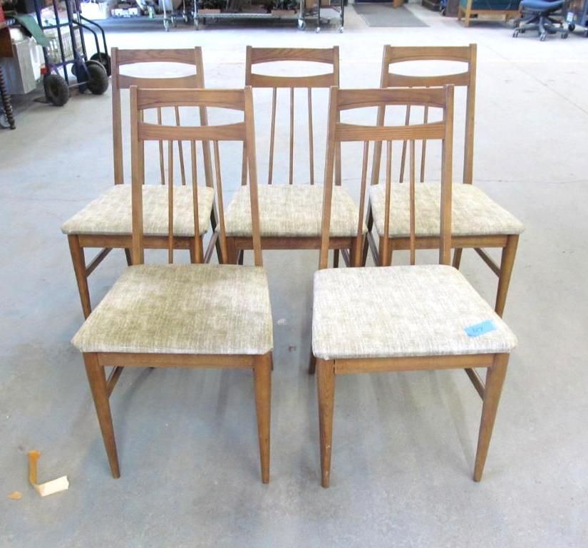 Six wooden dining chairs with light fabric seats in a room.