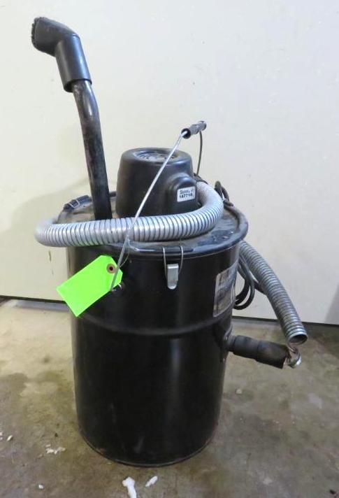 Black industrial vacuum cleaner with a metal hose, on a concrete floor.