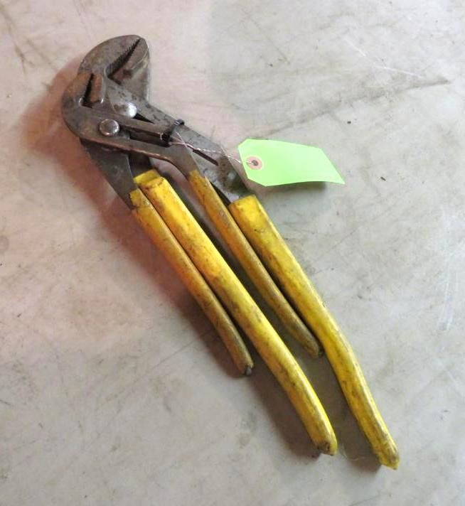 Yellow-handled adjustable pliers on a light-colored surface; a green tag is attached.