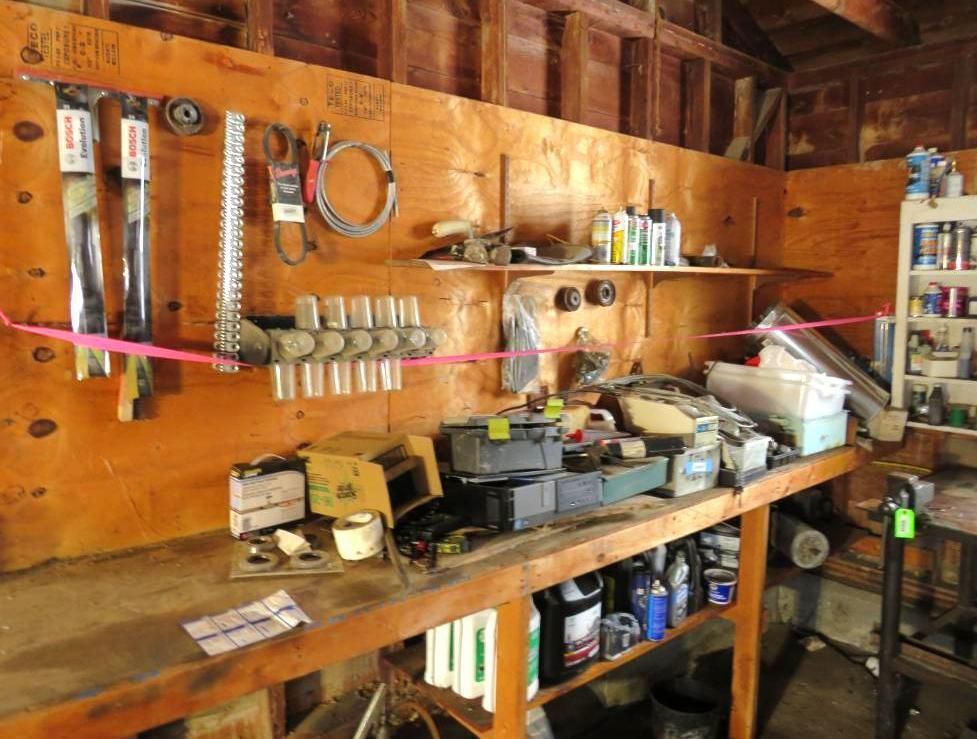Workshop with tools, parts, and supplies on a wooden workbench and shelves against a plywood wall.