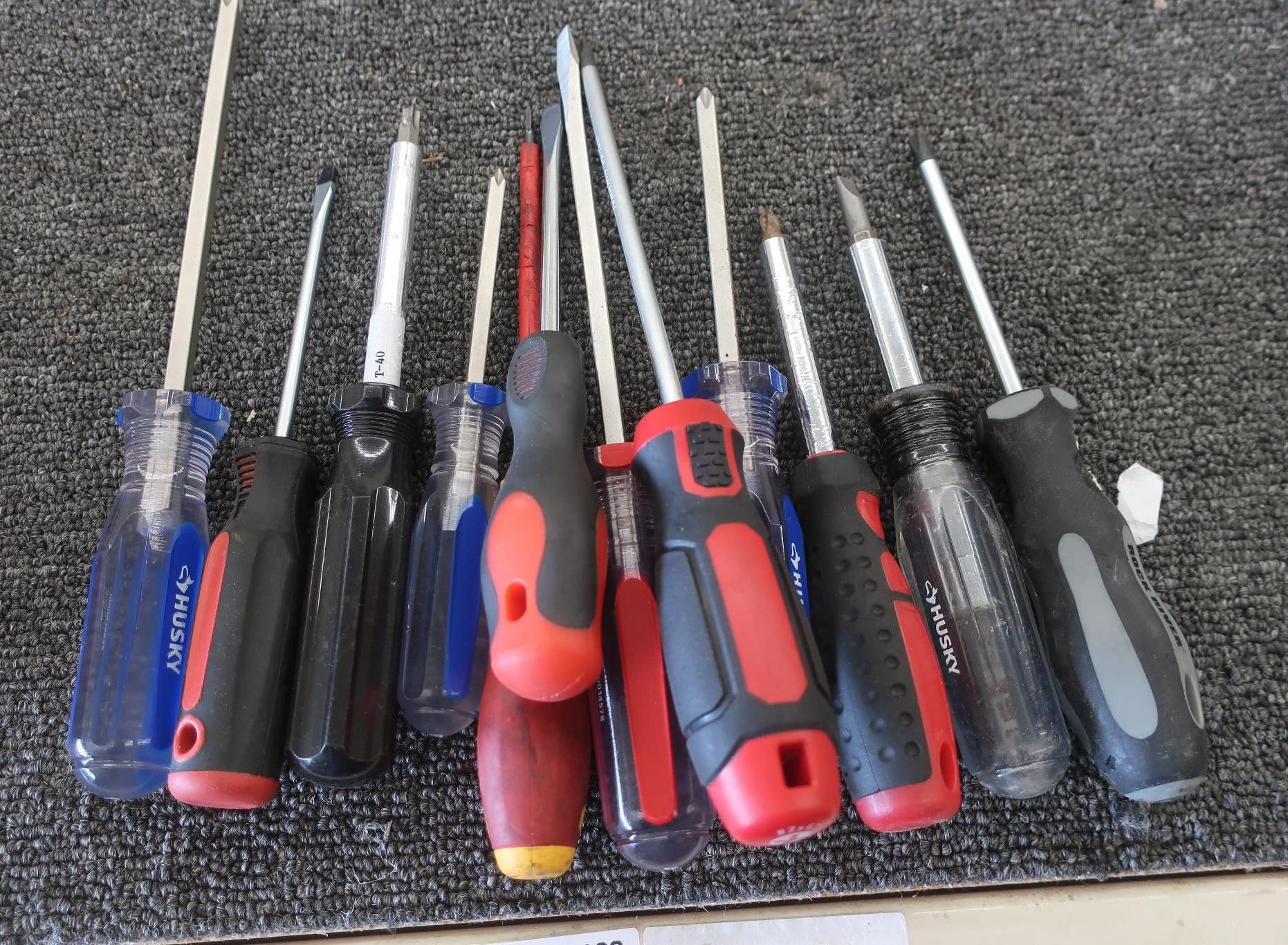 Assorted screwdrivers with various handle colors on a dark surface.