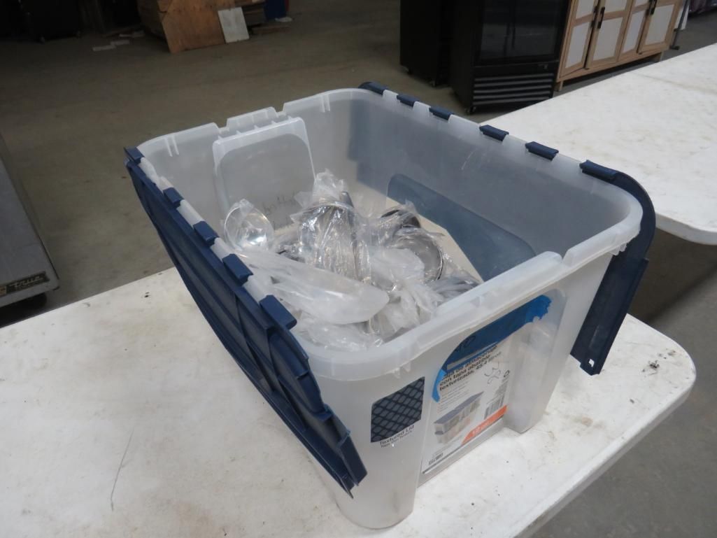 A clear plastic storage bin with blue accents contains items, sitting on a white table in a warehouse.