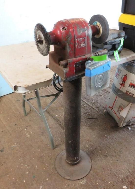 Red and black bench grinder on a pedestal stand, with two wheels and power cord.