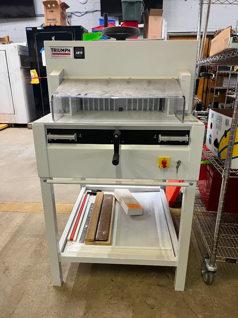 White paper cutter machine with safety guard, on a white metal stand.