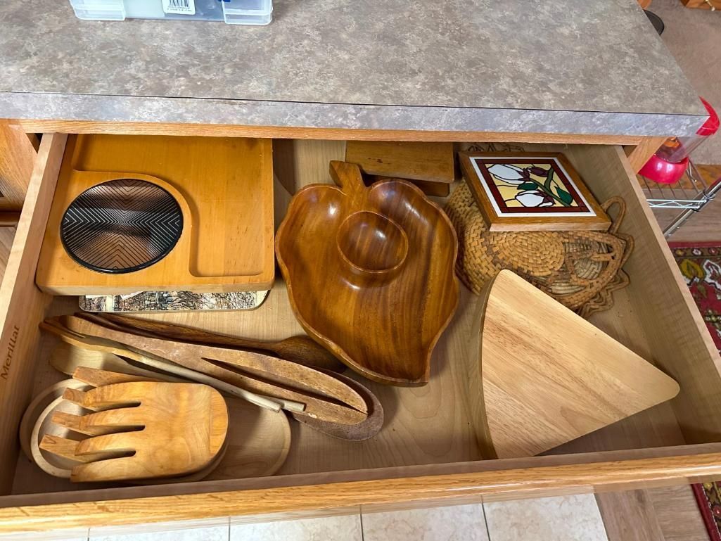 Open kitchen drawer with wooden serving items and a tile.