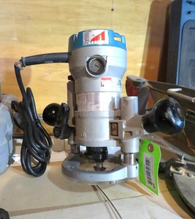 A silver and blue router with black handles and a power cord, sitting on a work surface.