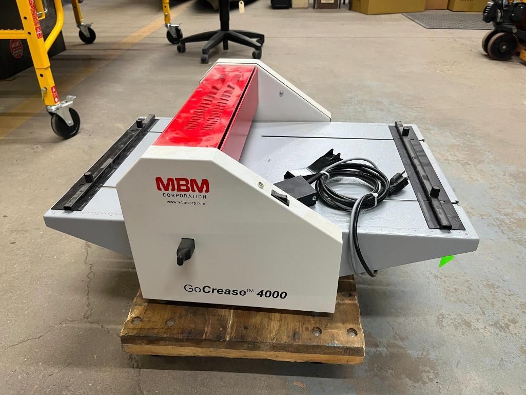 An MBM Cutter T-4600 paper cutter machine on a wooden pallet in a workshop. It is white with a red top.