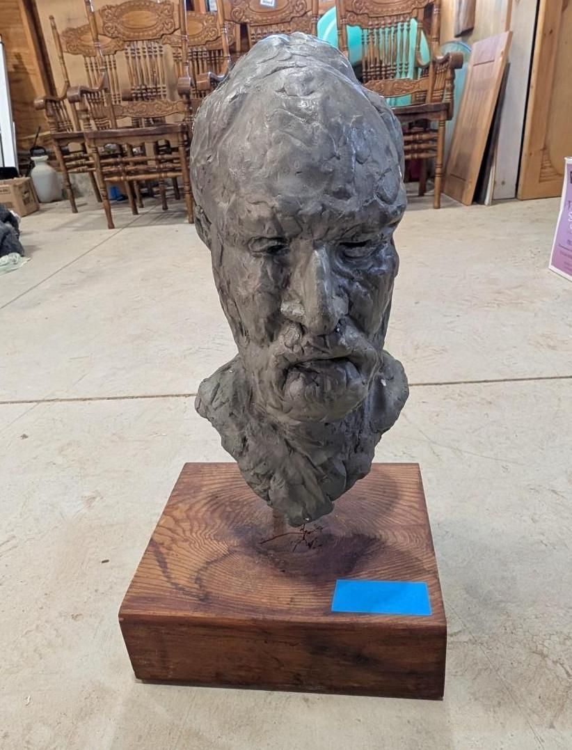 Bronze bust sculpture on a wooden base in a workshop or studio setting