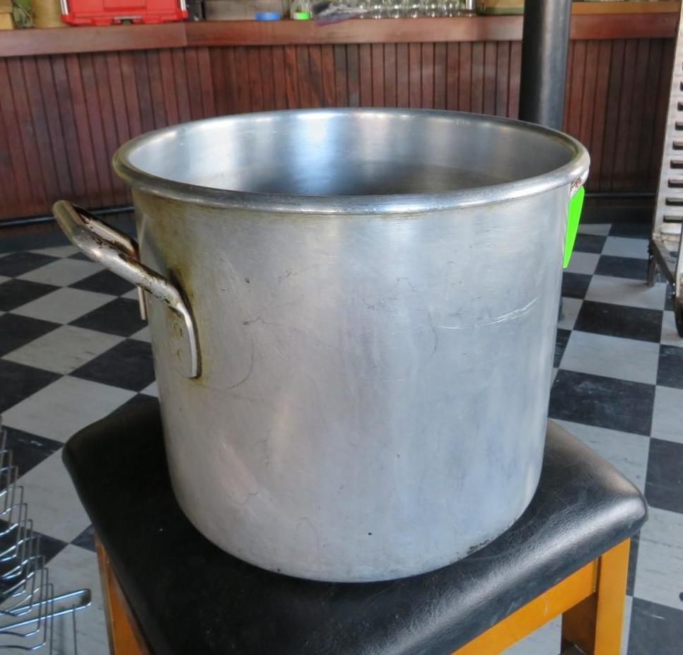 Large, silver metal pot with handles, sitting on a black stool. Checked floor in background.